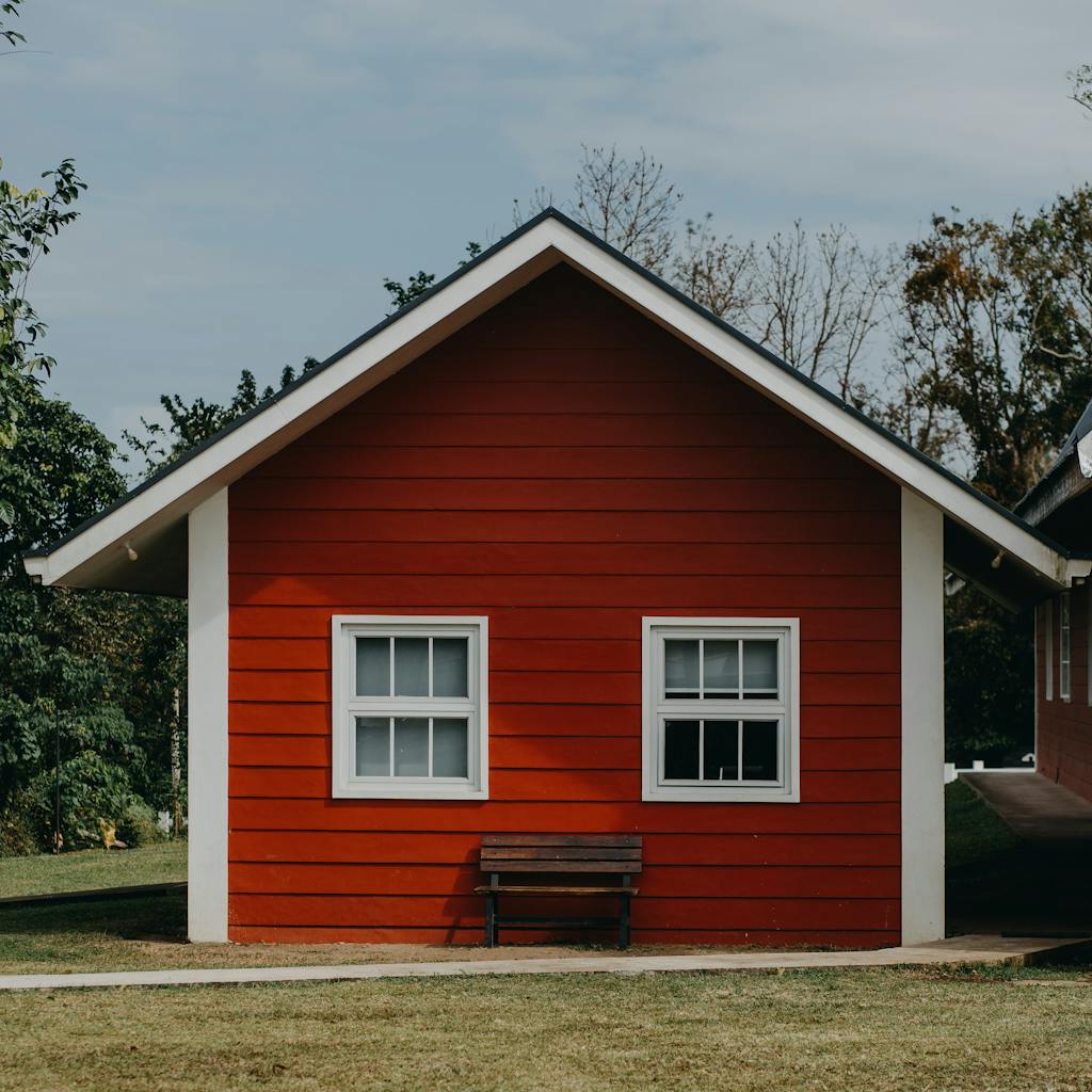 A vibrant red bungalow facade with windows and a bench in a serene outdoor setting in the Philippines.